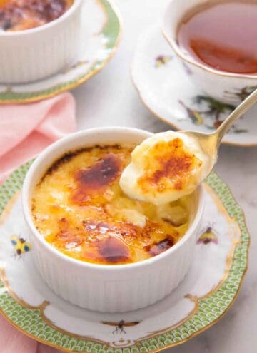 A spoonful of crème brûlée lifted from the ramekin with a cup of tea in the background.