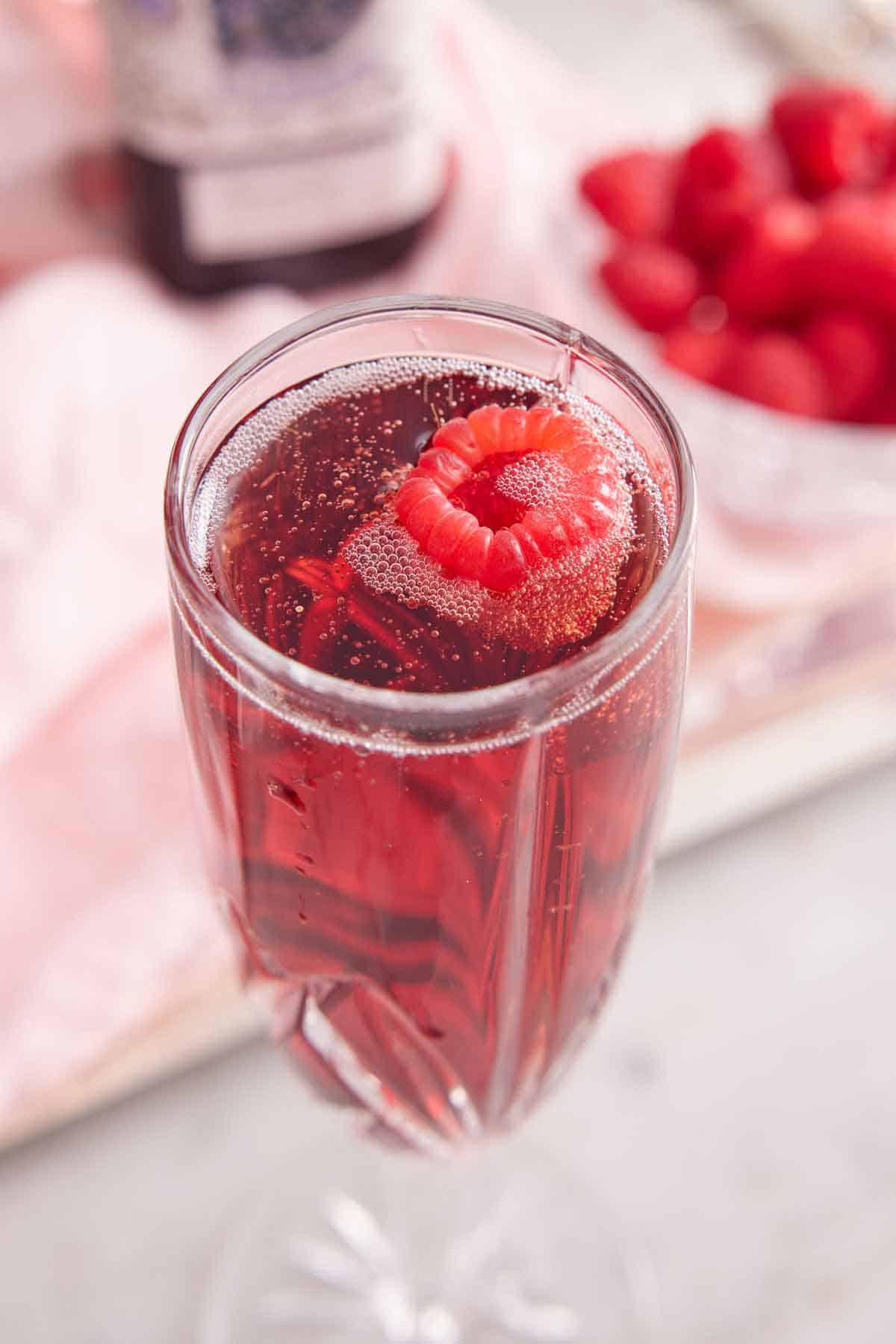 A glass of Kir Royale with a fresh raspberry floating on top.