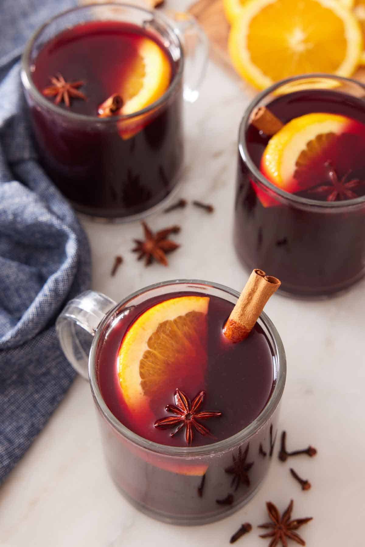 Slightly overhead view of three glasses of mulled wine garnished with cinnamon stick, orange slice, and star anise.