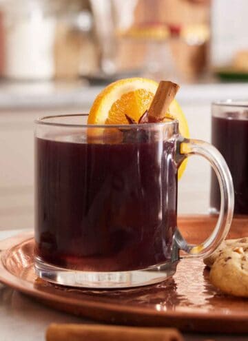 A glass of mulled wine with a cinnamon stick and orange slice garnish.