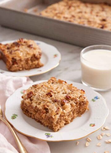 Two plated slices of oatmeal cake with a glass of milk and rest of the baking pan in the background.