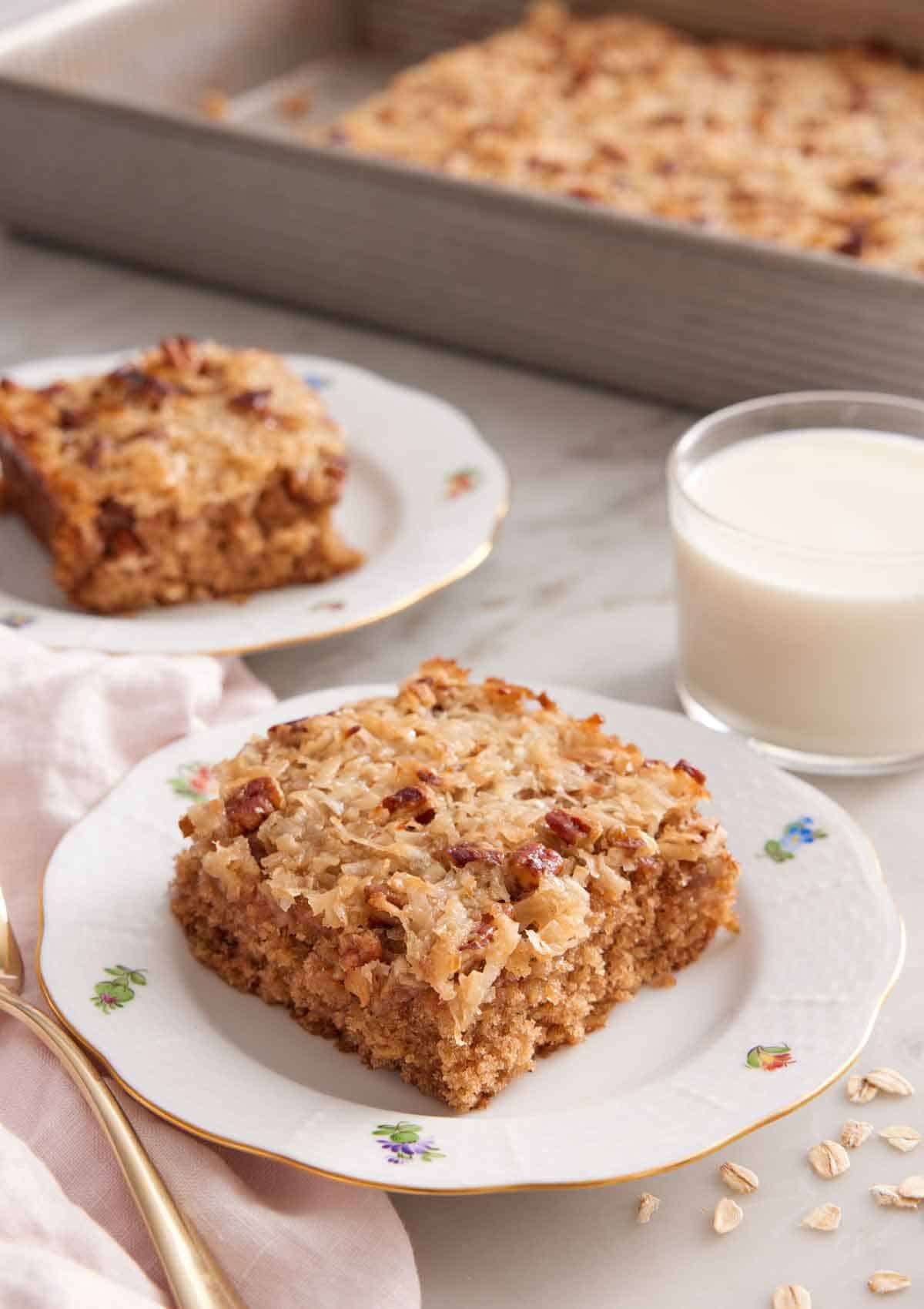 Two plated slices of oatmeal cake with a glass of milk and rest of the baking pan in the background.
