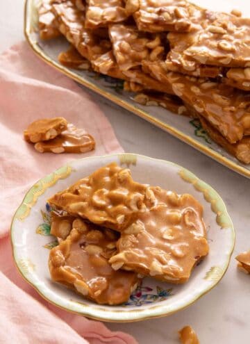 A plate of peanut brittle with a platter with more in the background.