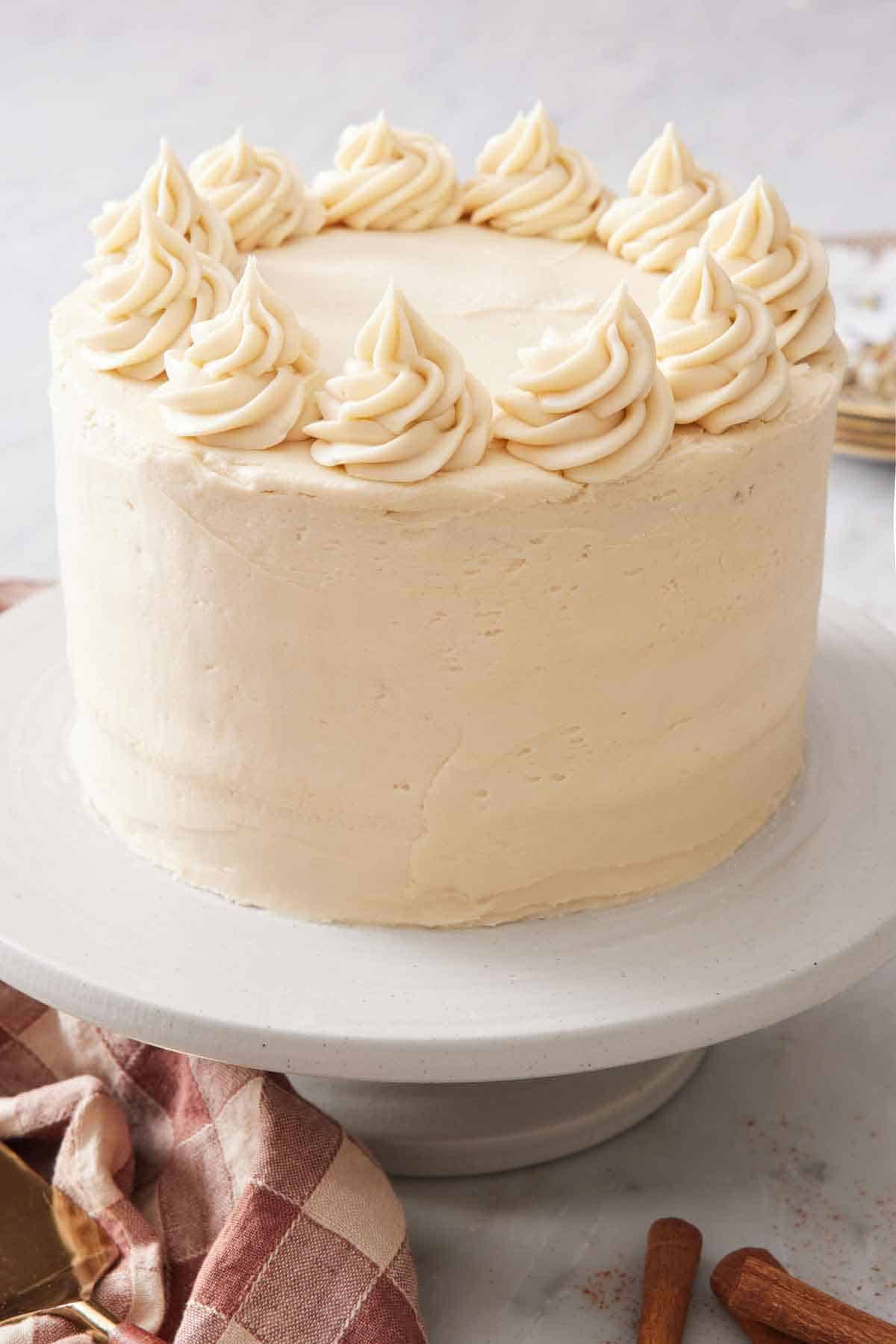 A frosted snickerdoodle cake with dollops of frosting around the edge of the cake on a cake stand.