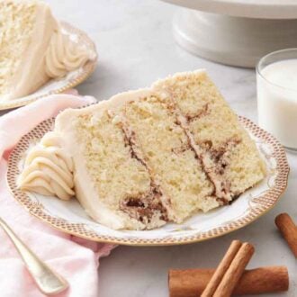 Two plated slices of snickerdoodle cake with a glass of milk and cinnamon sticks scattered around.