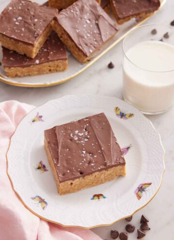 A plate with a Special K bar with a glass of milk and platter of more bars in the background.