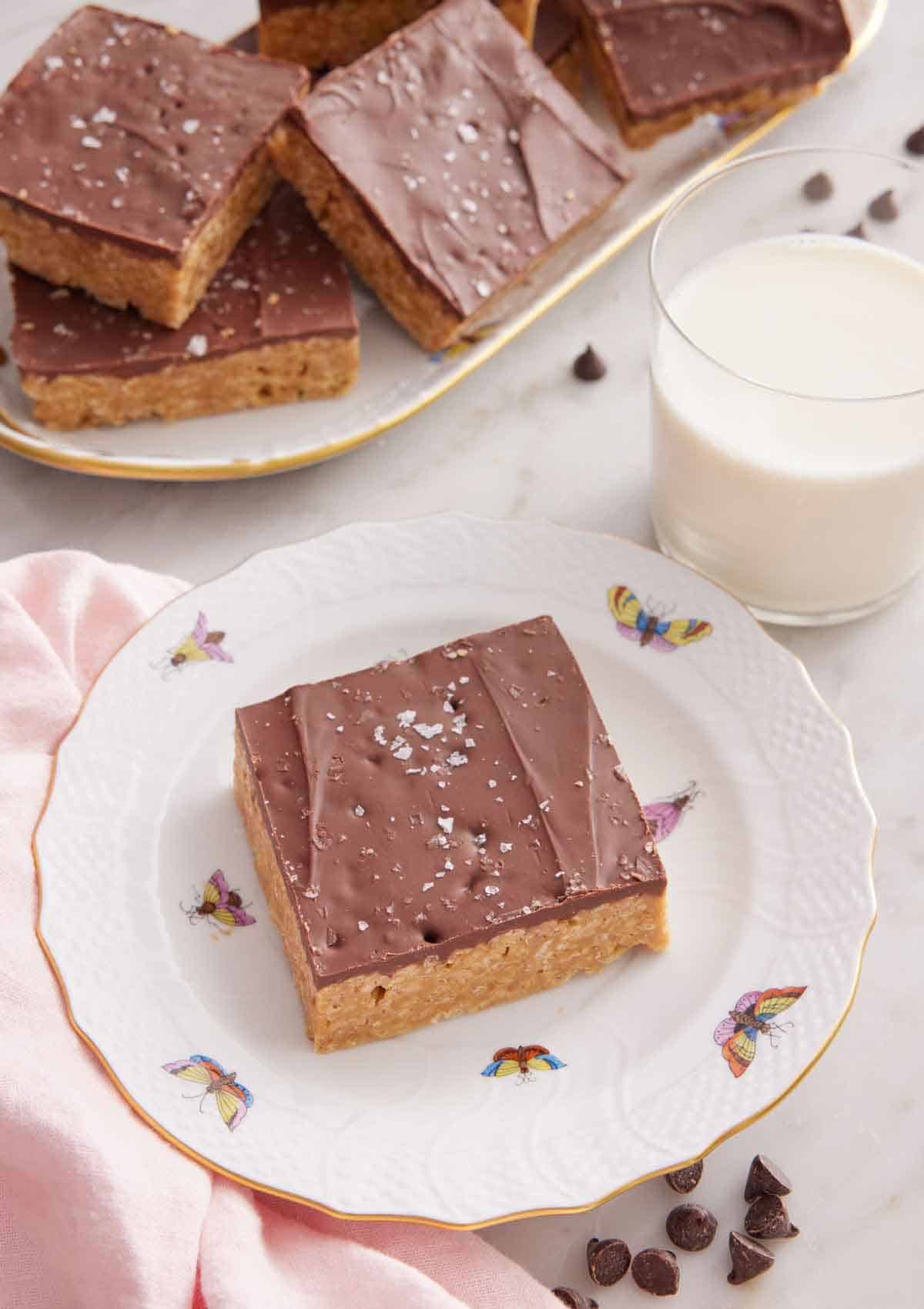 A plate with a Special K bar with a glass of milk and platter of more bars in the background.