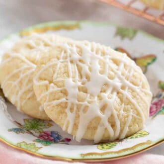 A plate with two lemon cookies with a glass of milk in the back.