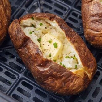 Three baked potatoes with butter and chives in an air fryer basket.