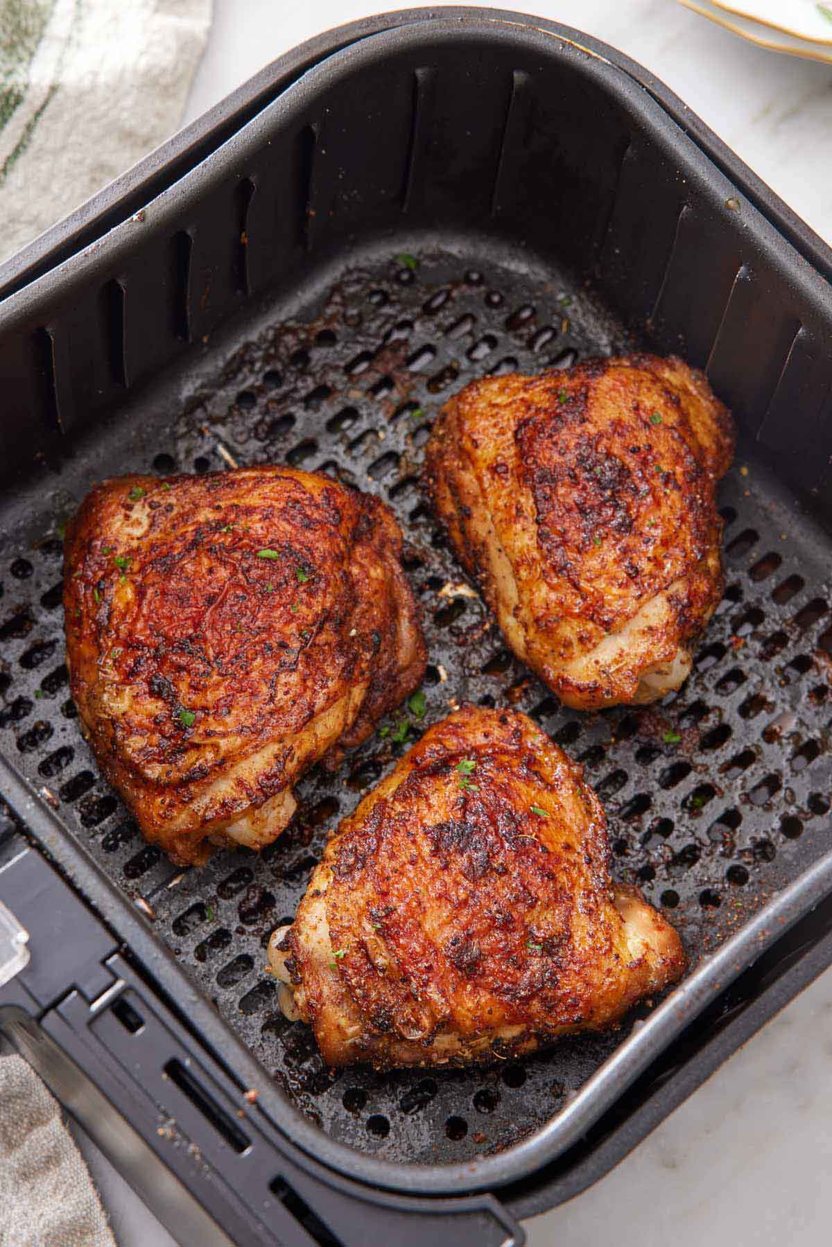 Three air fryer chicken thighs in an air fryer basket.