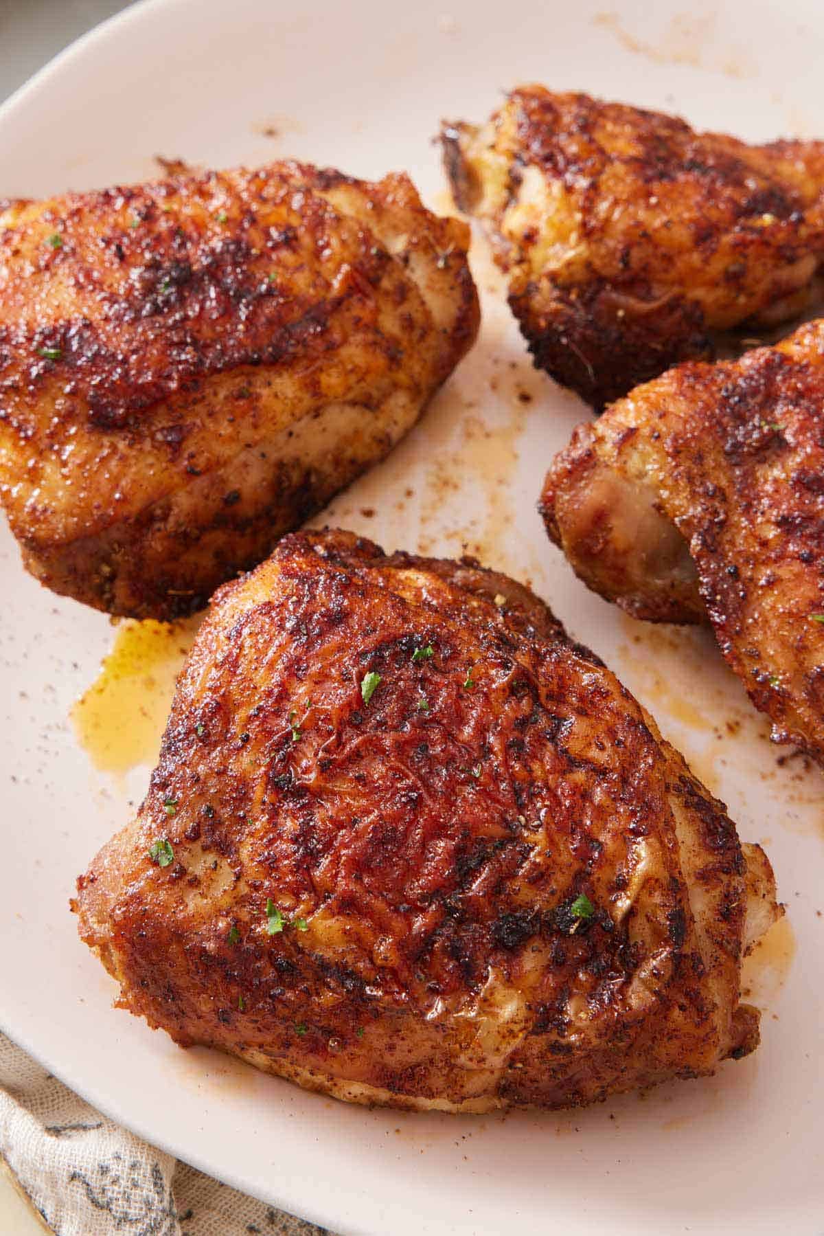 A plate with four air fryer chicken thighs with some chopped herb garnish.