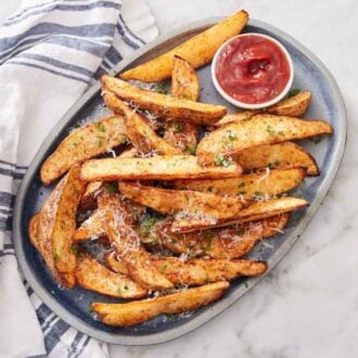 Overhead view of a platter of air fryer potato wedges topped with parsley and parmesan with a bowl of ketchup.