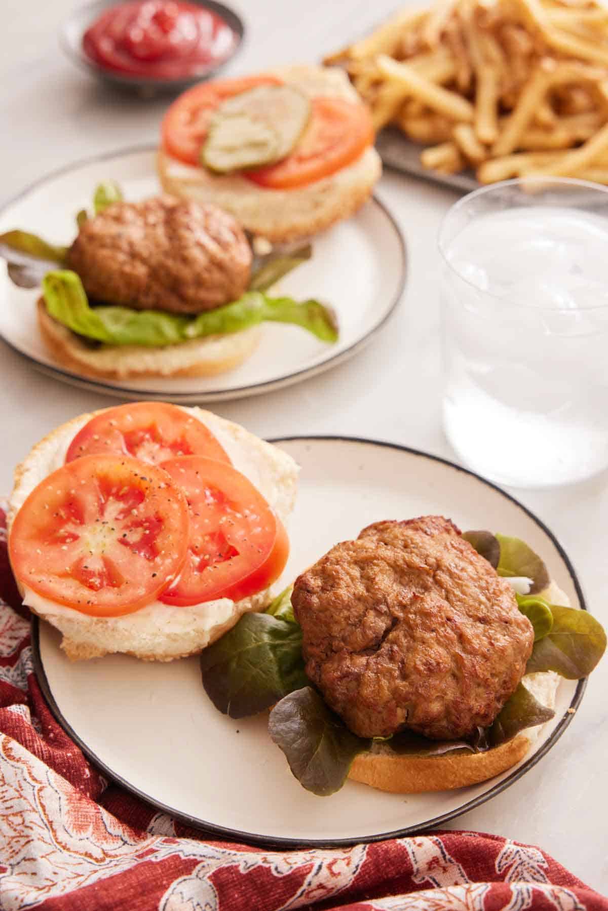 A plate with an opened face air fryer turkey burger with a glass of water in the back along with additional plate and a platter of fries.