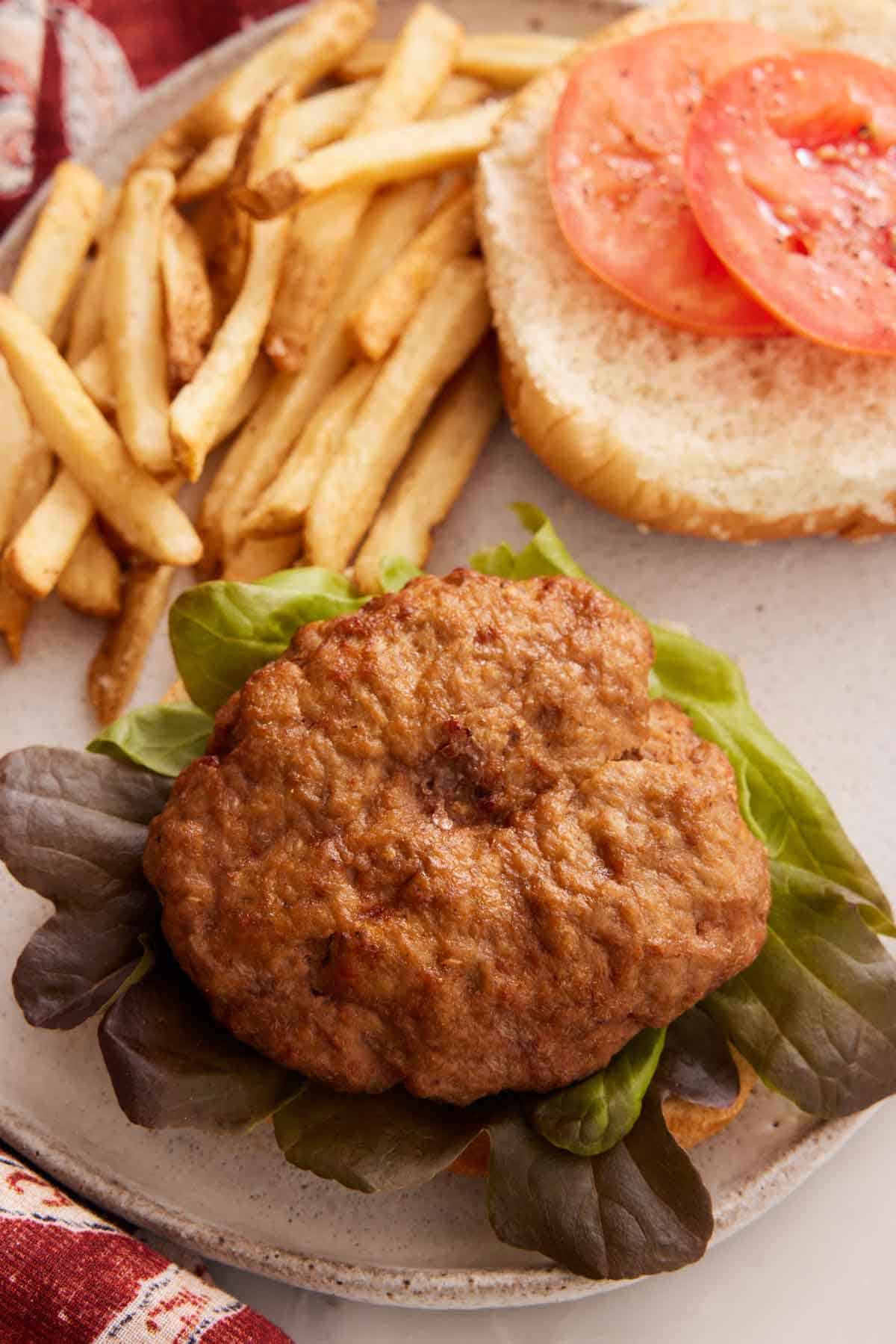 An air fryer turkey patty on top of lettuce and a bun. Fries in the back along with tomatoes on a top bun.