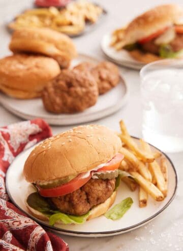 A plate of air fryer turkey burger with fries on the side with a glass of water in the background along with more burger ingredients.