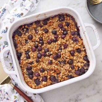 Overhead view of a baking dish of baked oatmeal with a napkin beside it along with a spatula and some plates off to the side.