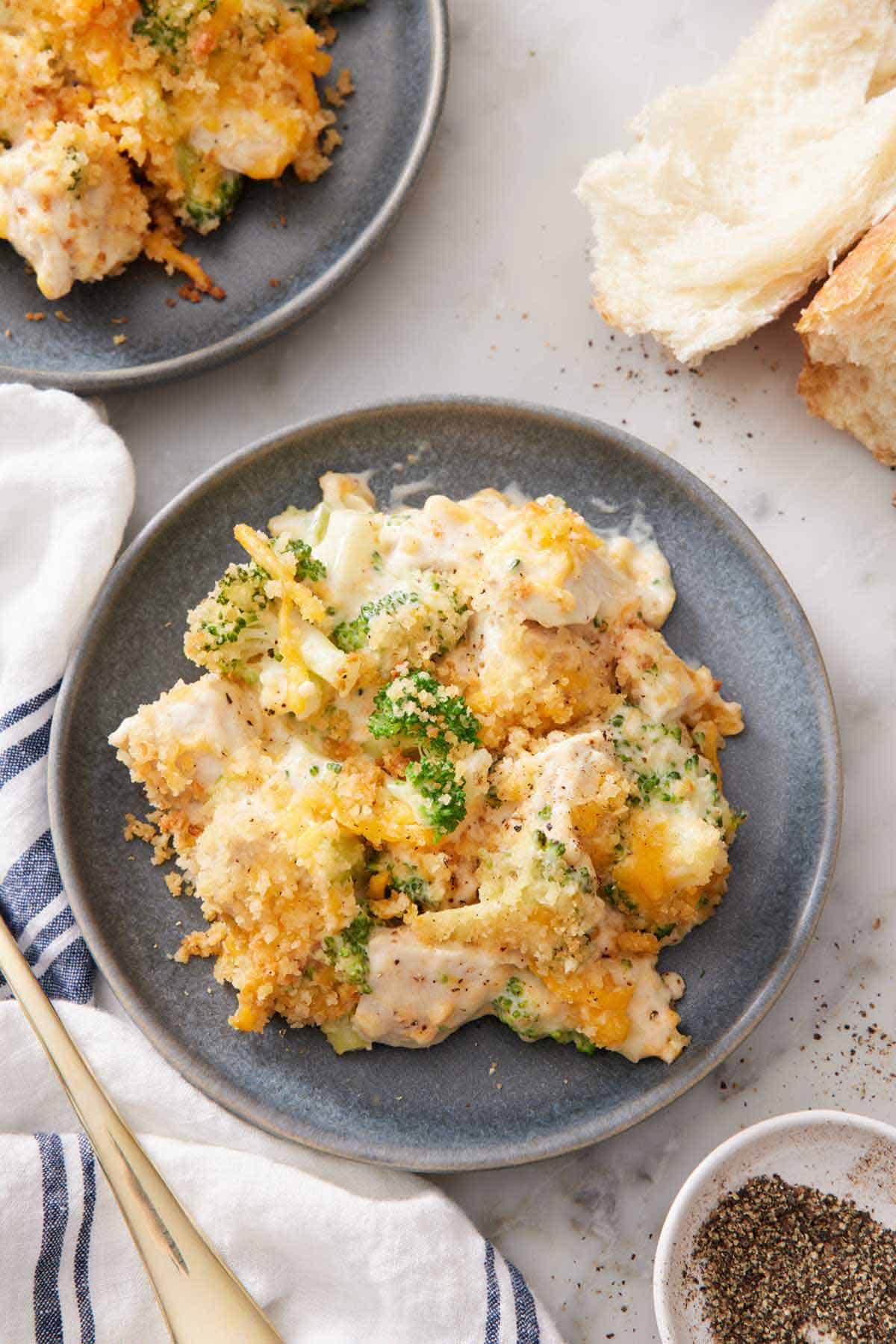 Overhead view of a plate of chicken divan with some torn bread on the side with a bowl of pepper.