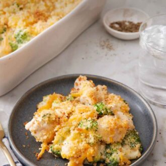 Pinterest graphic of a plate with a serving of chicken divan. A baking dish with more in the back along with a glass of water and bowl of pepper.