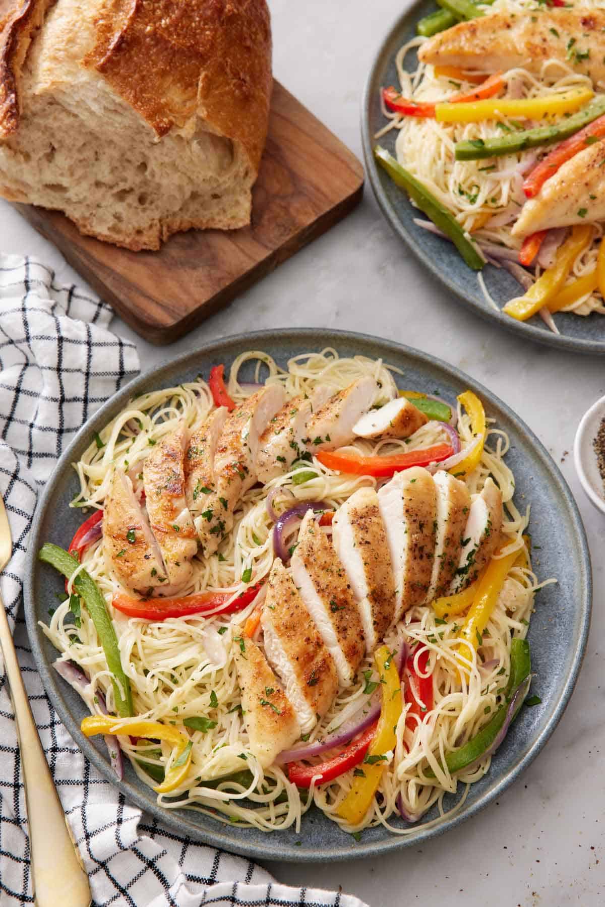 A plate of chicken scampi with two chicken tenderloins sliced on top. A plate with more and a loaf of bread in the background.