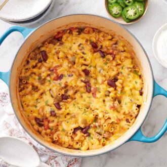 Overhead view of a pot of chili mac with a bowl of sour cream off to the side and jalapeño.