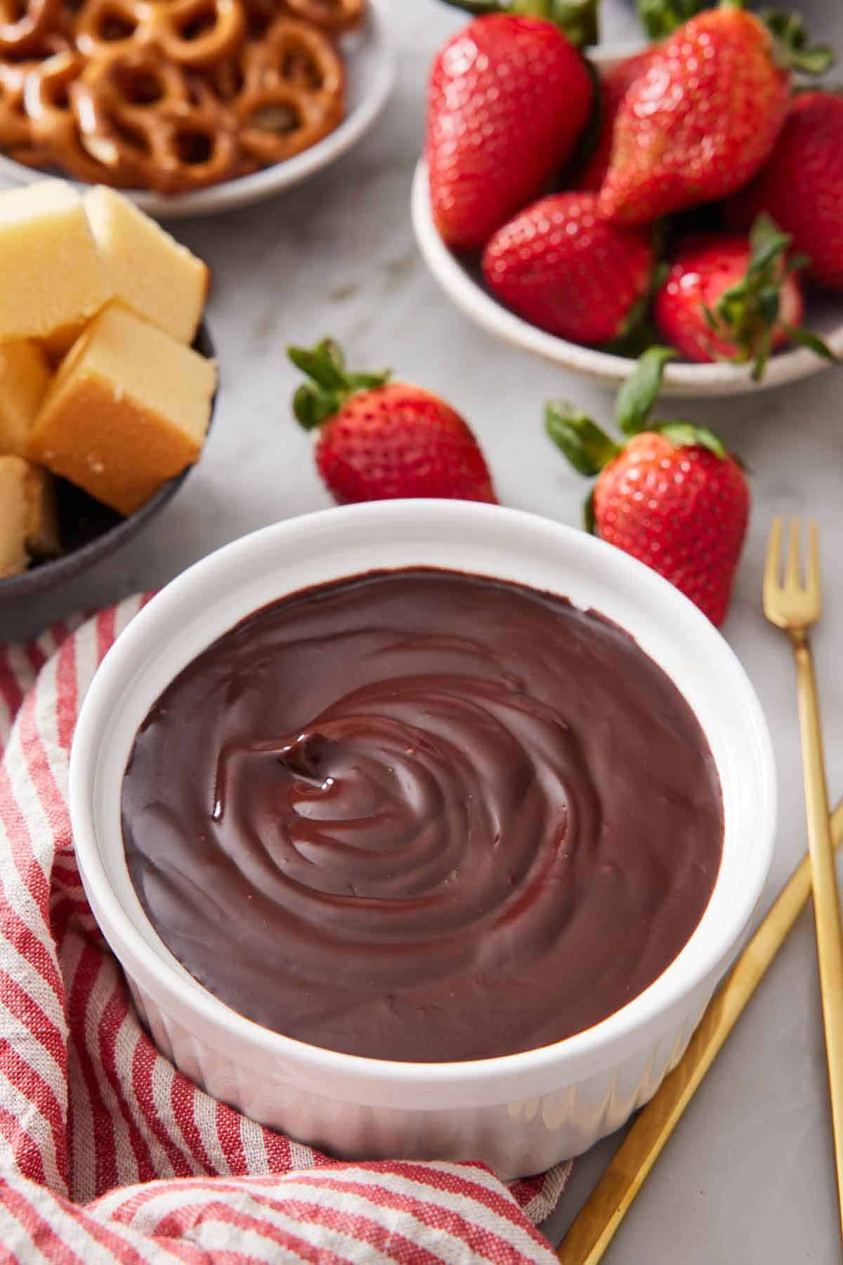 A bowl of chocolate fondue with assorted dippers in the background.