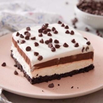 A plate with a slice of chocolate lasagna with a bowl of chocolate chips in the background.