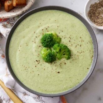 Overhead view of a bowl of cream of broccoli soup topped with broccoli florets and pepper on top.