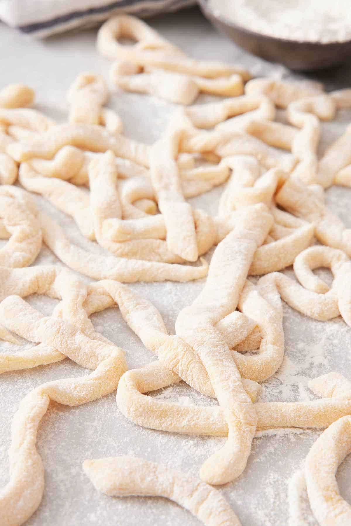 Multiple uncooked egg noodles tossed in flour on a counter.