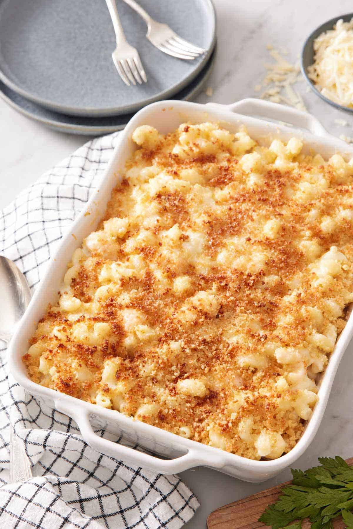 A baking dish of lobster mac and cheese with toasted breadcrumbs on top. Stack of plates and forks in the background.