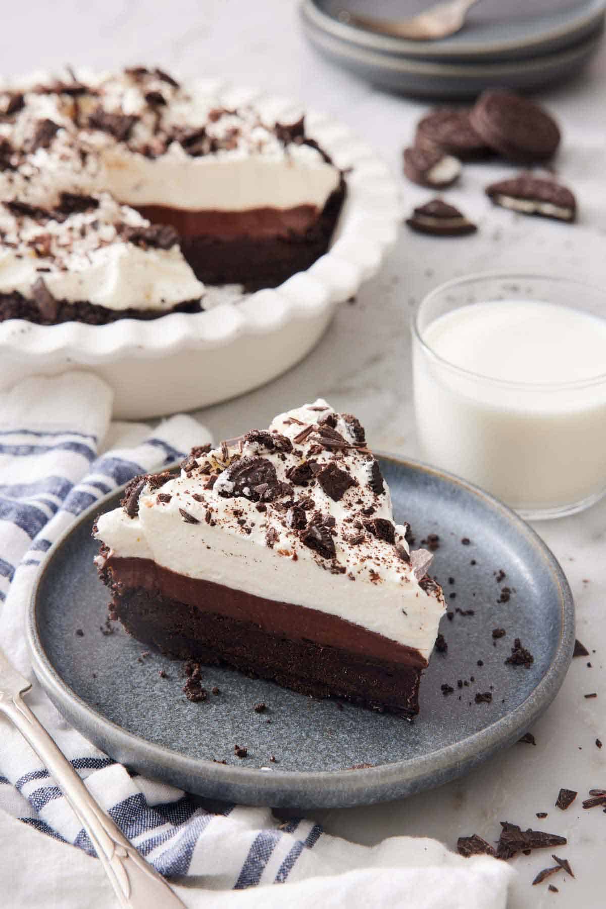 A slice of mud pie on a plate with a glass of milk and the rest of the pie behind it.