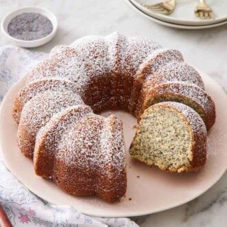 A platter of poppy seed cake with a slice cut out and a second slice cut but not removed.
