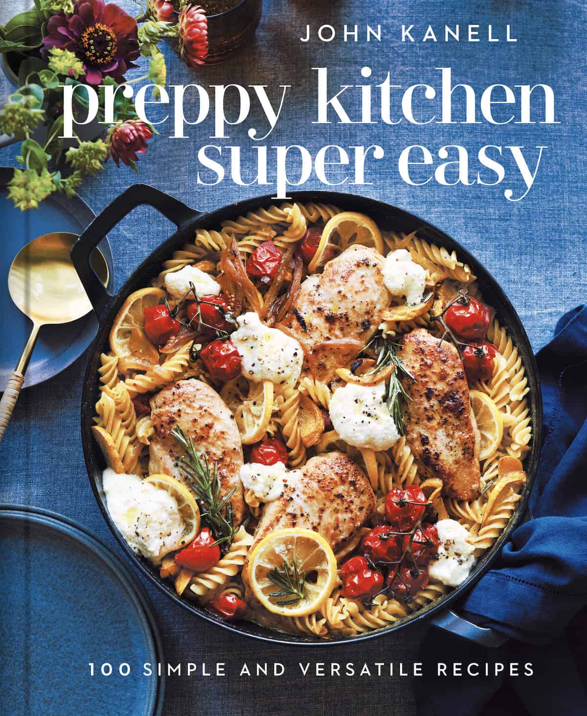 A photo of the new Preppy Kitchen Cookbook with a skillet of chicken, pasta and tomatoes on a blue background.