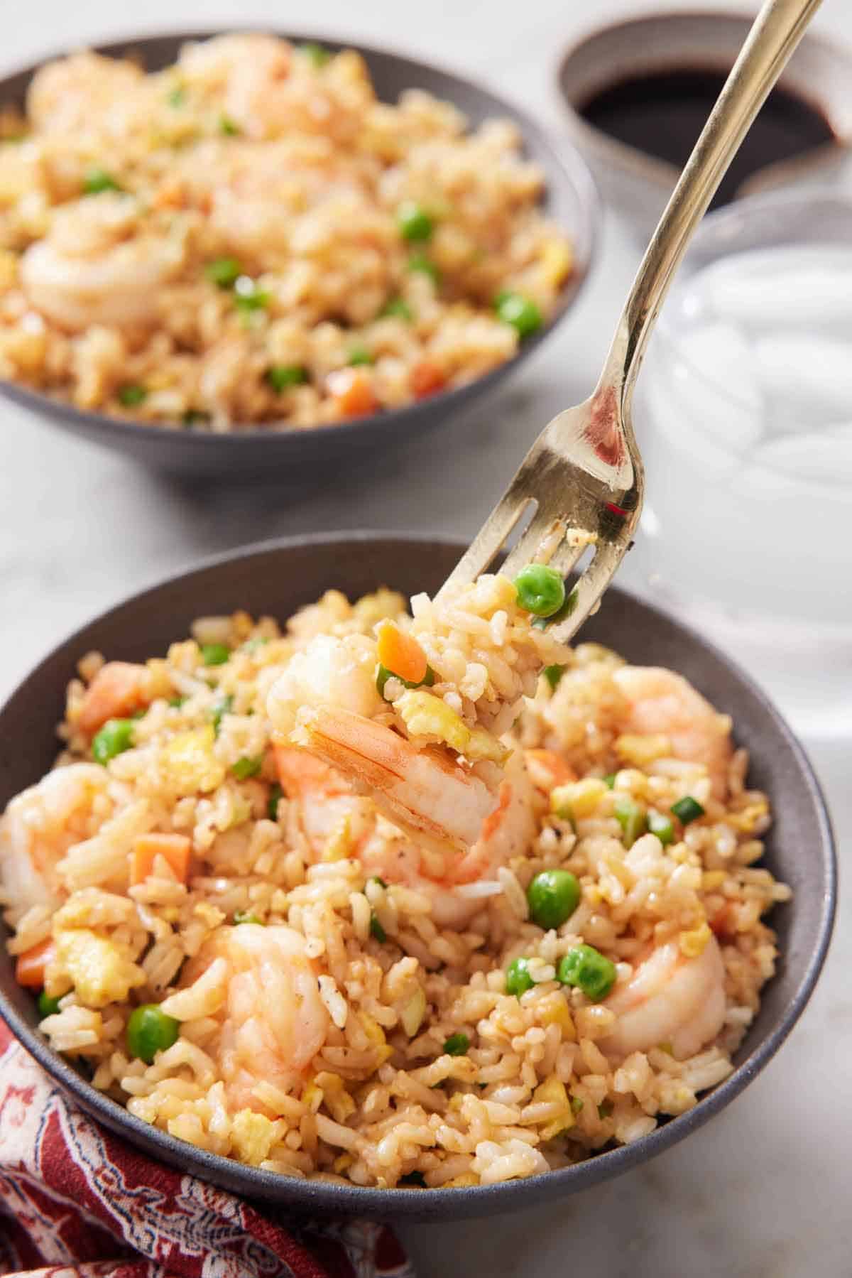 Two bowls of shrimp fried rice with a fork lifting up a bite from one bowl.