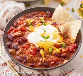 Pinterest graphic of a bowl of turkey chili with sour cream, two chips, shredded cheese, and green onions on top.