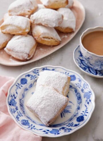 A plate with two air fryer beignets with a platter in the background along with a cup of coffee.