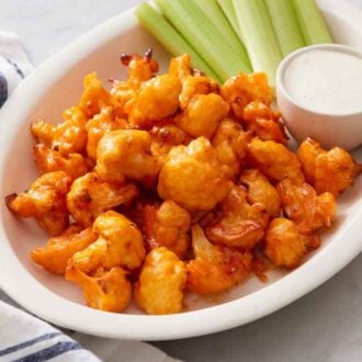 An oval platter of air fryer buffalo cauliflower with dip and celery sticks.
