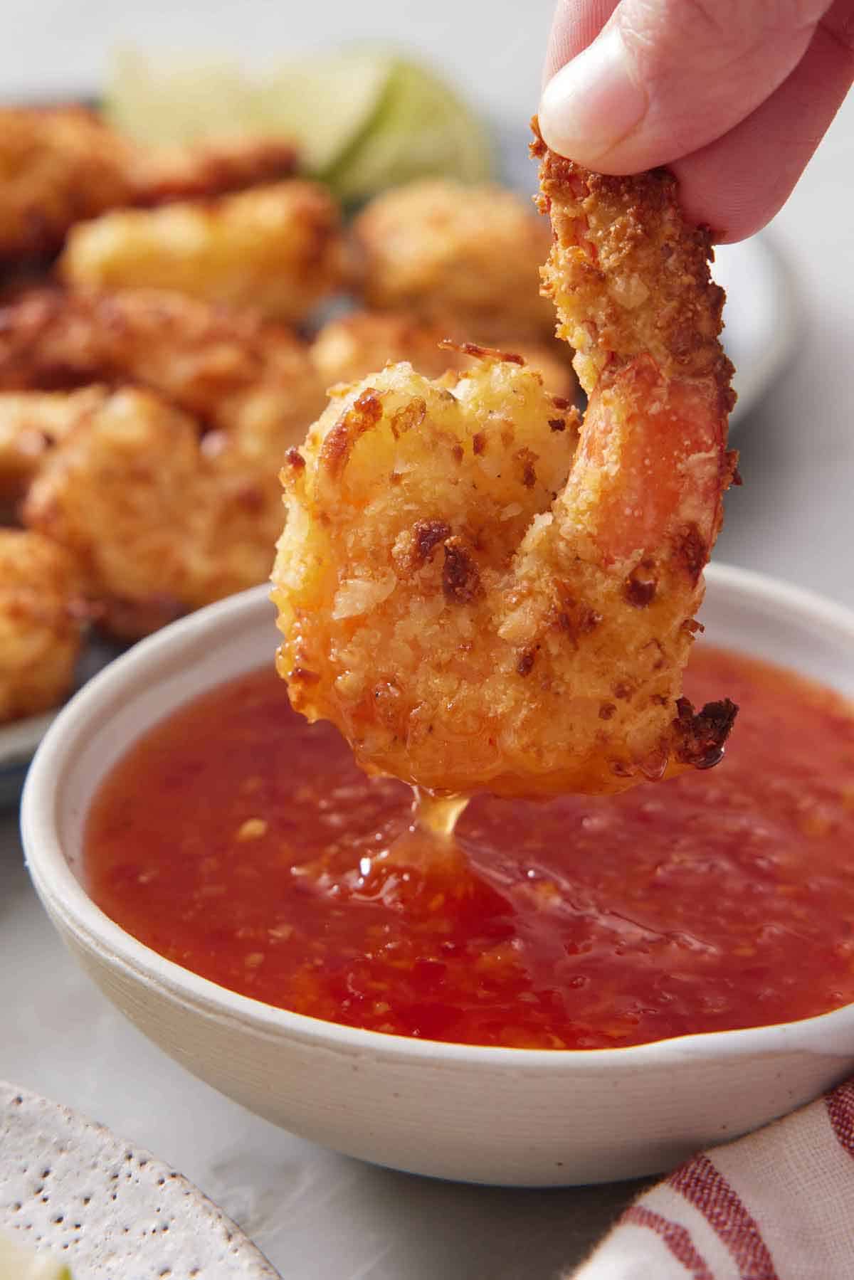 An air fryer coconut shrimp dipped into a bowl of sweet chili sauce.