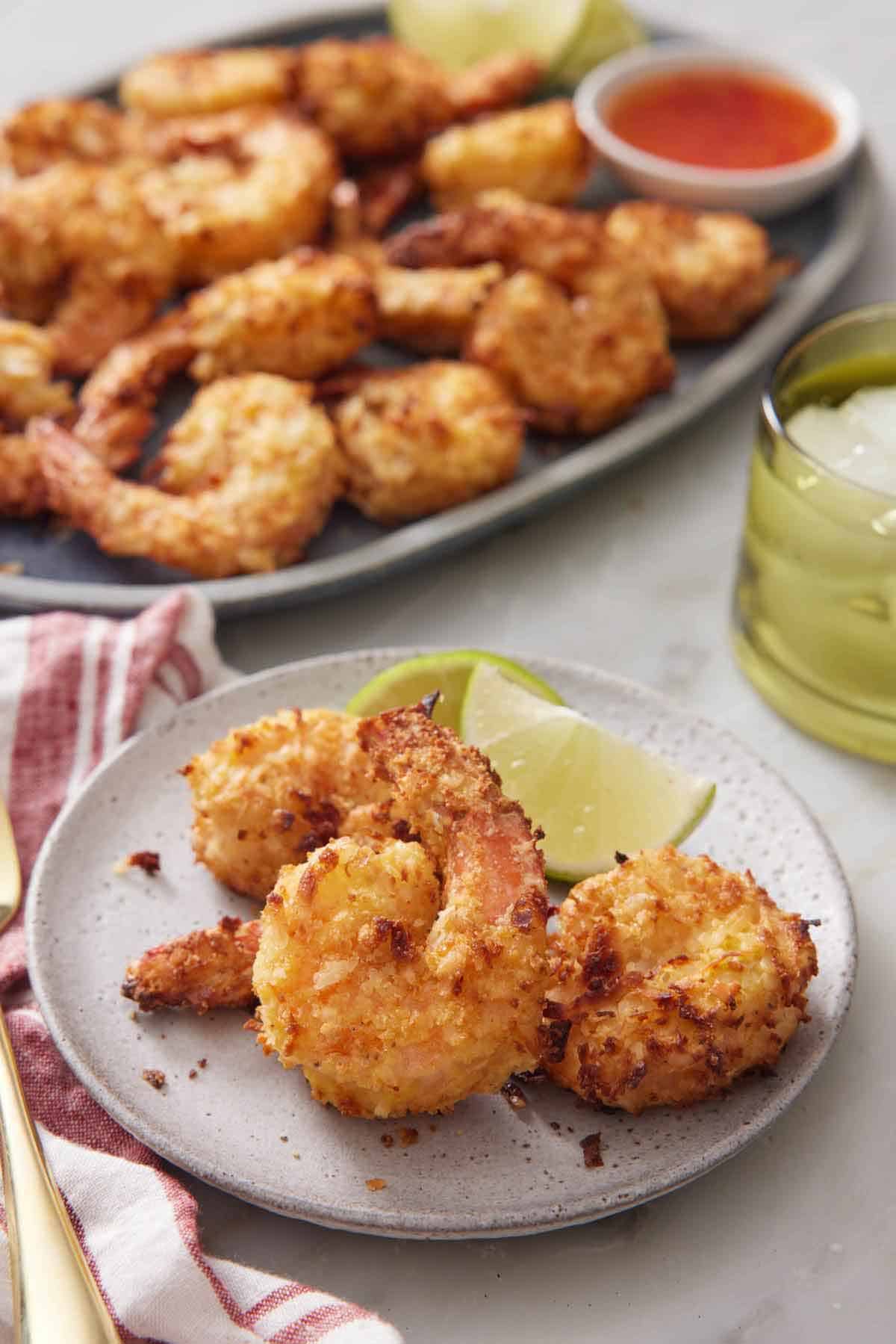 A plate of air fryer coconut shrimp with lime. A platter with more shrimp in the background.