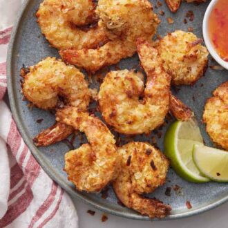 Overhead view of a plate of air fryer coconut shrimp with two lime wedges and sweet chili sauce.