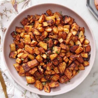 An overhead view of a plate of breakfast potatoes topped with chopped rosemary on top. A plate of bacon on the side with a spoon.
