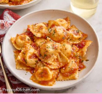 Pinterest graphic of a plate of cheese ravioli tossed in tomato sauce along with a glass of white wine.