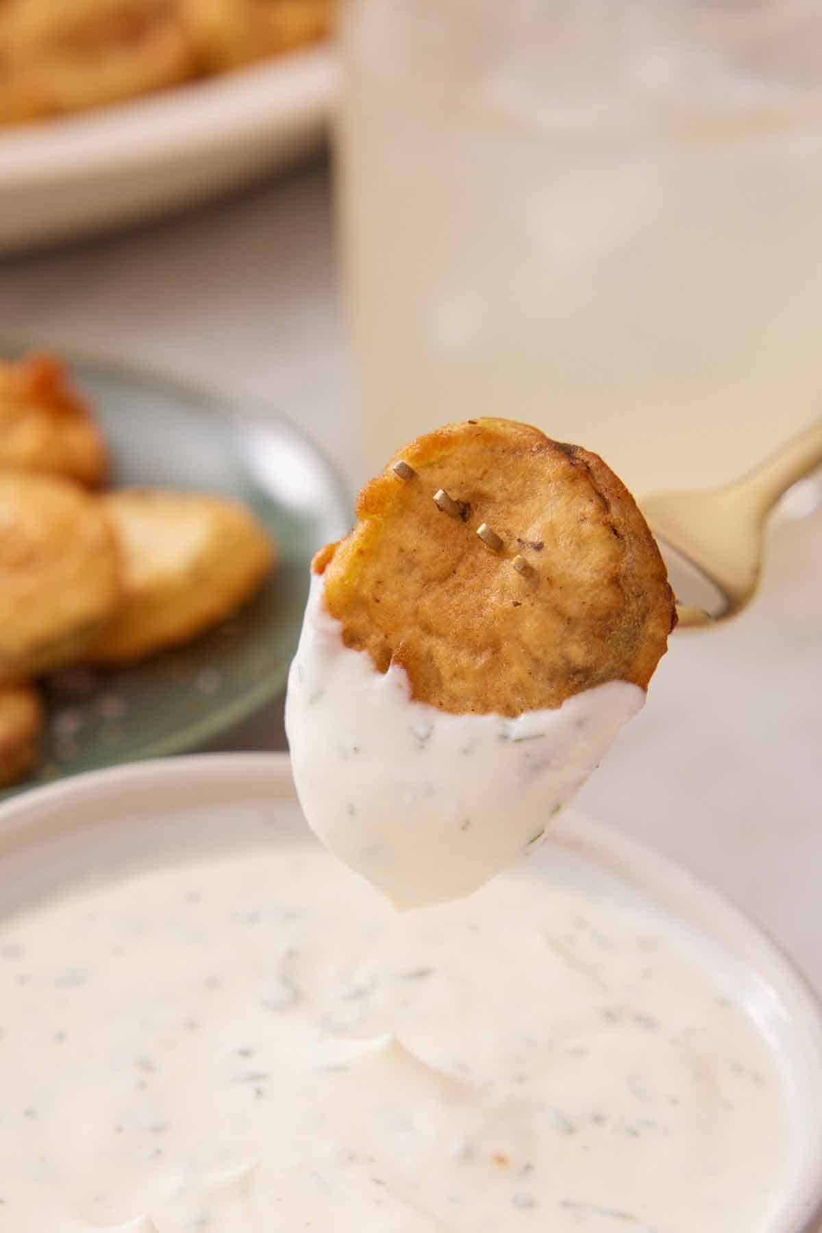 A fork with a fried pickle dripped in sauce.
