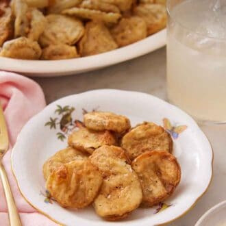 Pinterest graphic of a plate of fried pickles with a drink and platter of more fried pickles in the background.