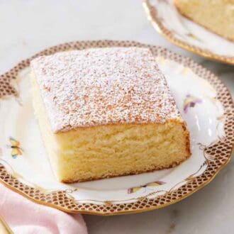 A plate with a slice of hot milk cake topped with powdered sugar with a fork beside it.