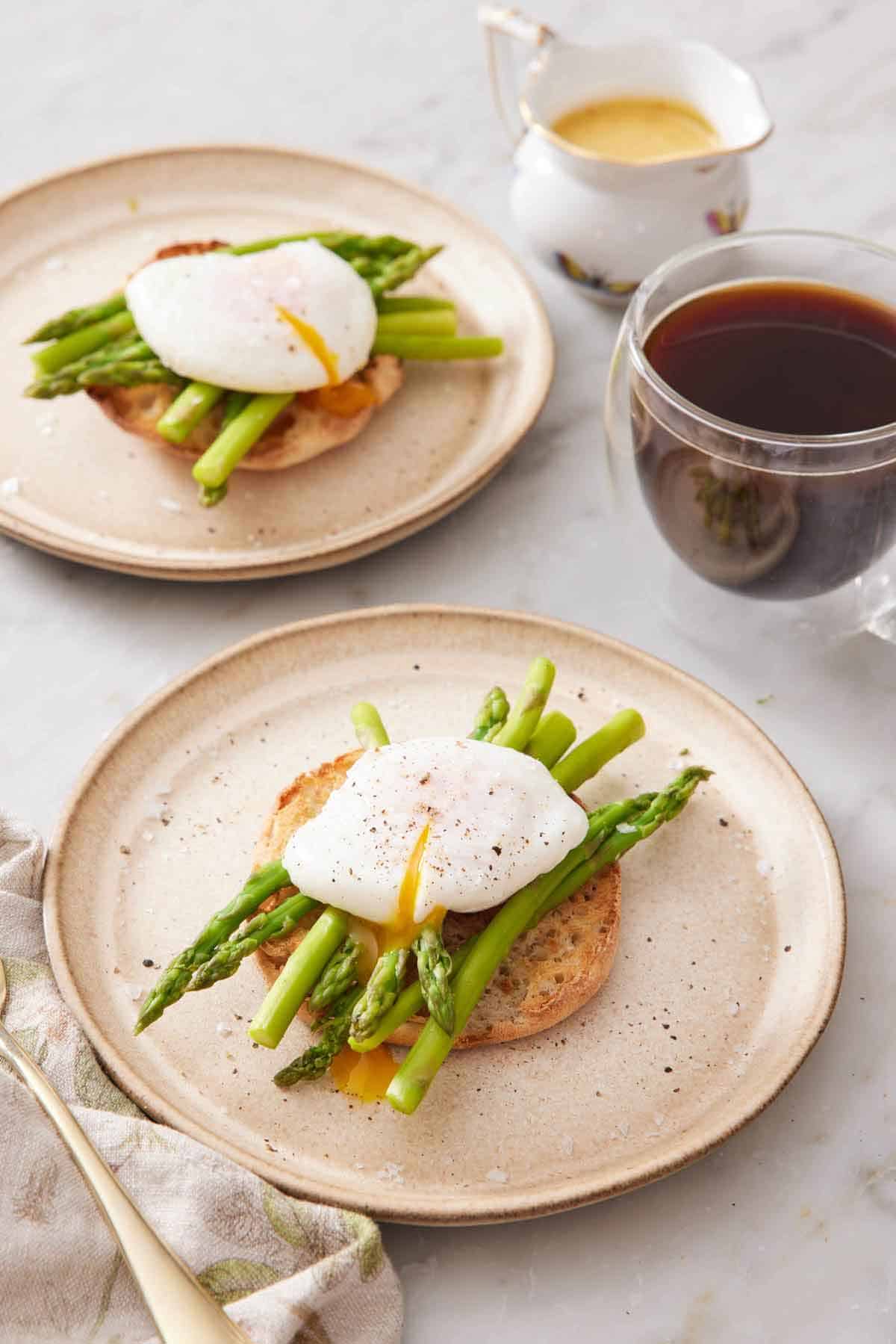 Two plates with a bagel topped with asparagus and a poached egg. A coffee and sauce off to the side.