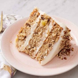 A plate with a slice of hummingbird cake with pecans on the frosting. A fork and glass of milk beside it.