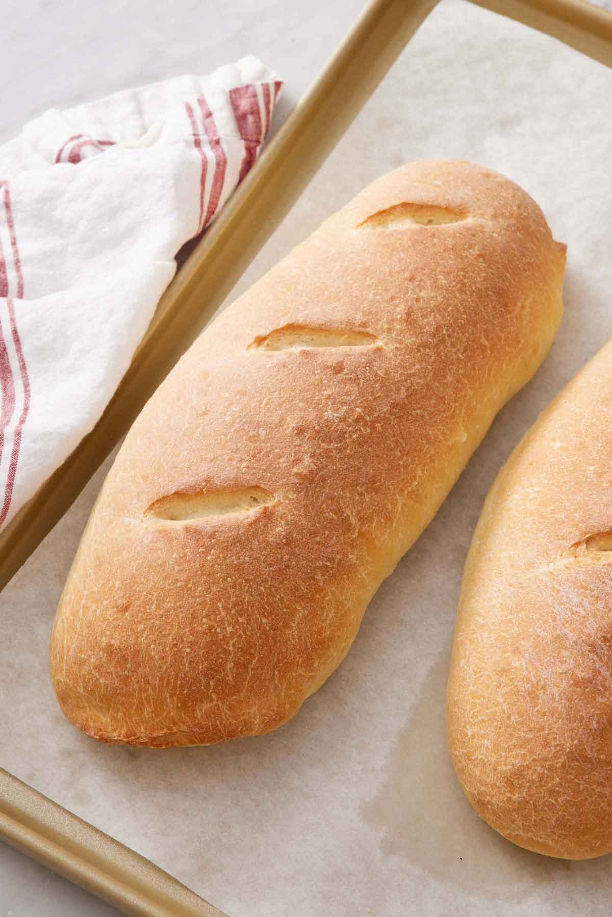 Overhead view of a lined sheet pan with two loaves of Italian bread, one slightly out of frame.