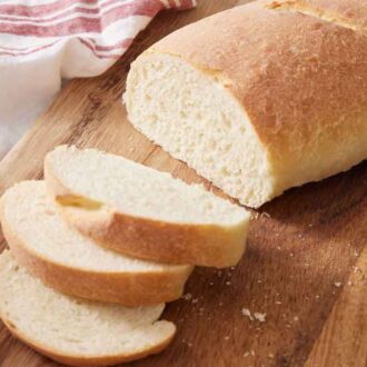 A loaf of Italian bread on a cutting board, three slices cut from it.