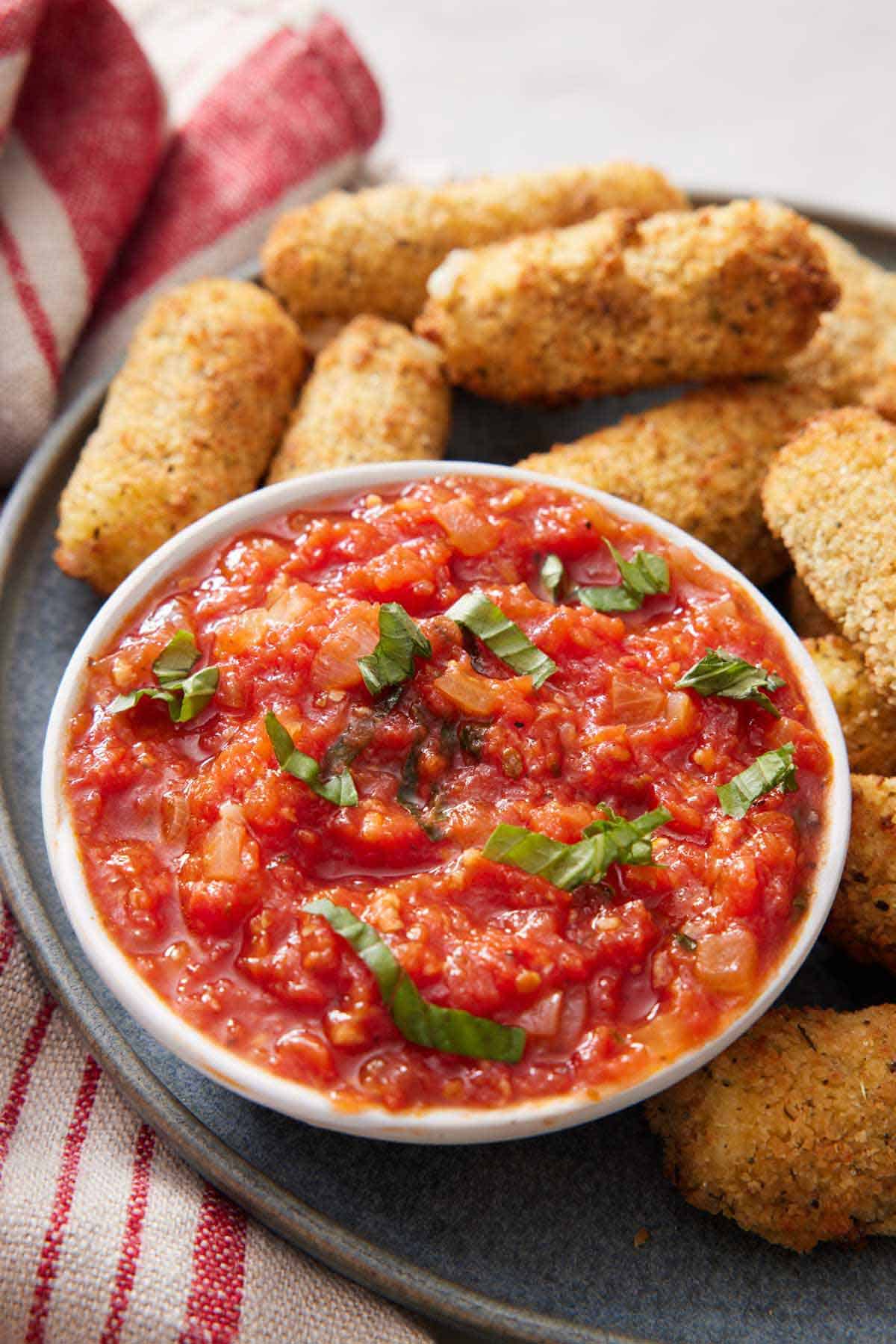 A bowl of marinara sauce topped with ribboned basil along with some mozzarella sticks.