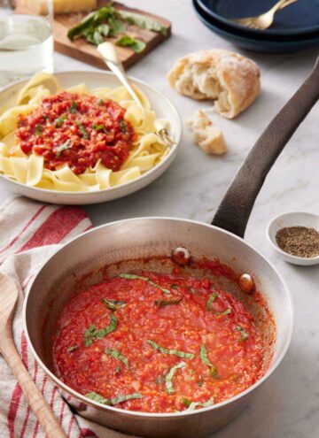 A pot of marinara sauce with torn bread in the back and a bowl of noodles with marinara sauce on top.